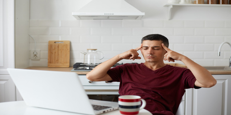 A man in the kitchen with a headache. Poor air quality in the home can cause headaches and discomfort.