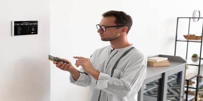A man uses a smartphone to remotely control a smart thermostat in his home.