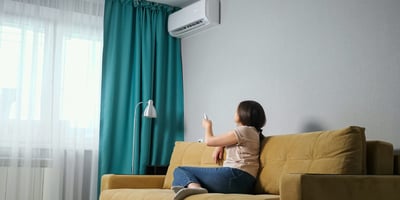 The woman controls the air conditioner in the living room with a remote control.