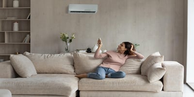 Woman sitting on sofa and restarting her air conditioner via remote control