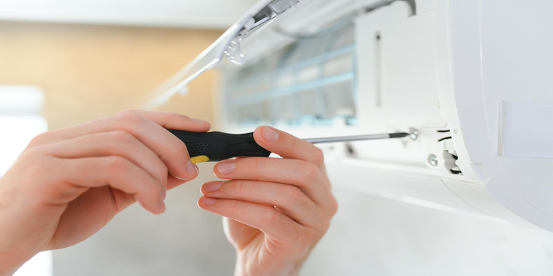 The master unscrews the screws of the indoor unit of the mini-split system using a screwdriver.