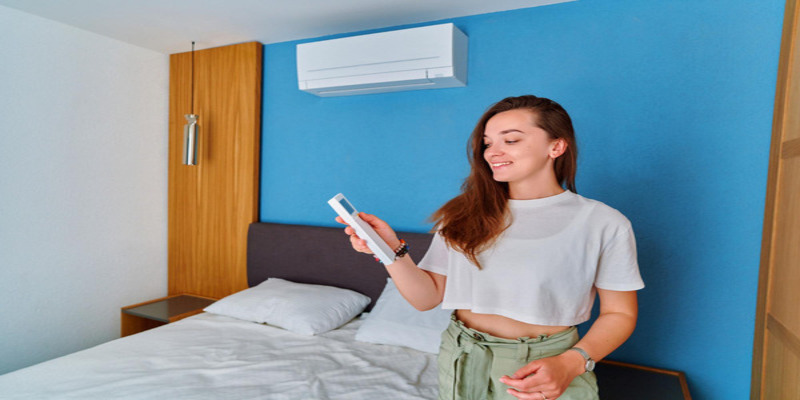 Woman adjusting air conditioner with remote control in bedroom with blue wall.