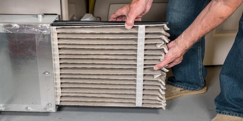 Person replacing a dirty air conditioner filter with a new one.