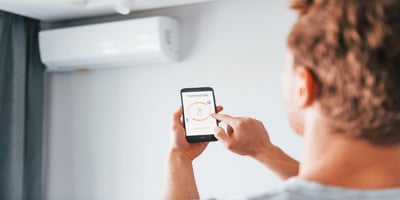 A man controls the temperature of the air conditioner via smartphone in a modern room.