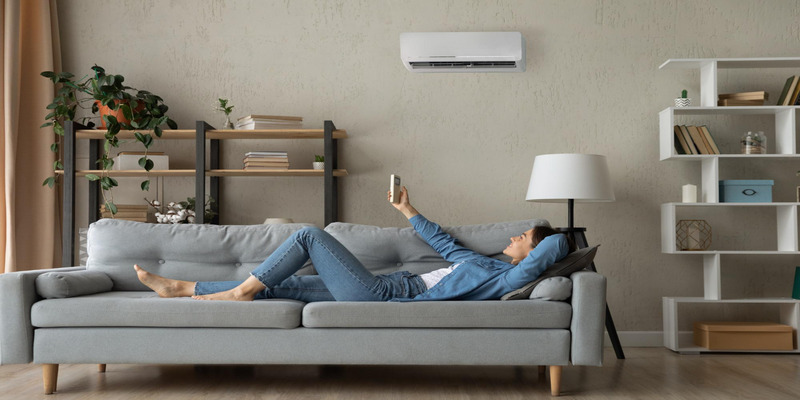 A person relaxing on a couch while using a smartphone to control the air conditioning system with Sensibo for maximum comfort and energy efficiency.