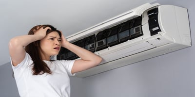Woman looking frustrated while standing under a malfunctioning air conditioner.