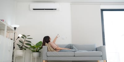 A woman comfortably sitting on a couch and adjusting the air conditioning temperature, demonstrating the convenience of controlling home climate remotely with Sensibo.