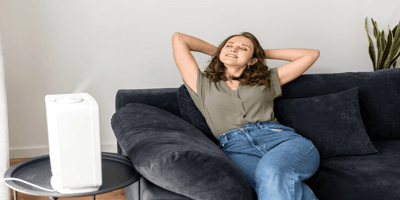 Woman relaxing on a couch with a Smart Air Purifier running nearby during allergy season.