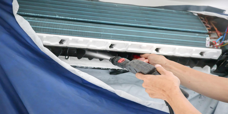 Technician cleaning air conditioner with water pressure