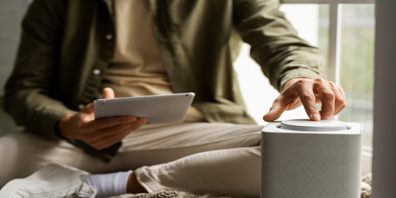 Man adjusting the settings on a compact air purifier while holding a tablet.
