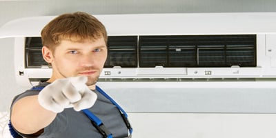 Technician pointing to AC unit, highlighting air conditioner lifespan and when to replace AC.