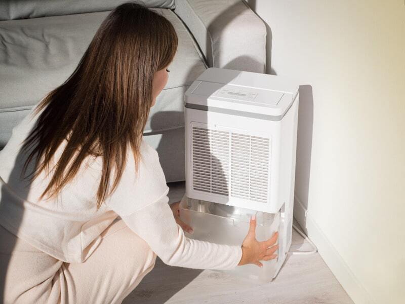 Woman using dehumidifier to lower humidity in house and improve humidity control