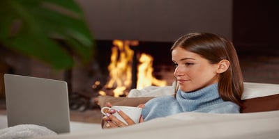 Woman relaxing at home by fireplace with optimal winter thermostat setting.