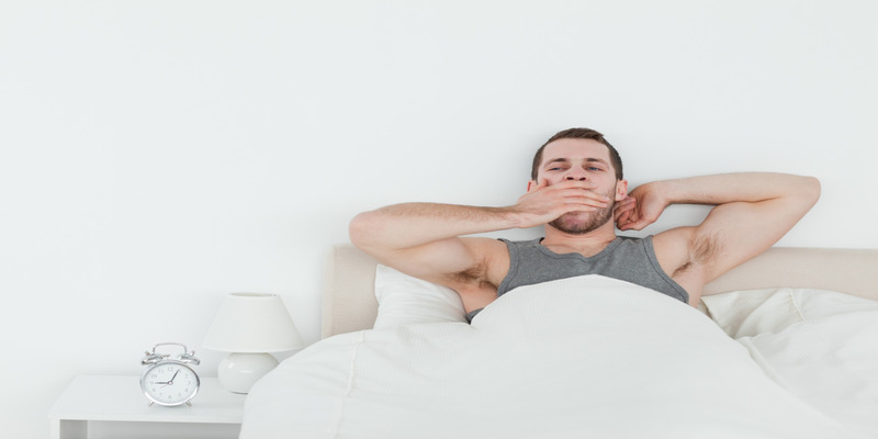 Man waking up tired and yawning in bed
