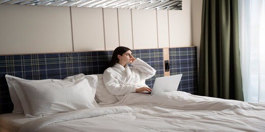 young-woman-working-her-laptop-while-sitting-bed-hotel-room_23-2149304021 (1)